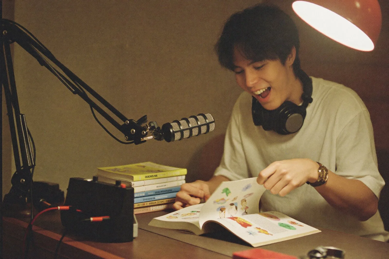 A young man with headphones around his neck in a small home studio with a microphone and picture books