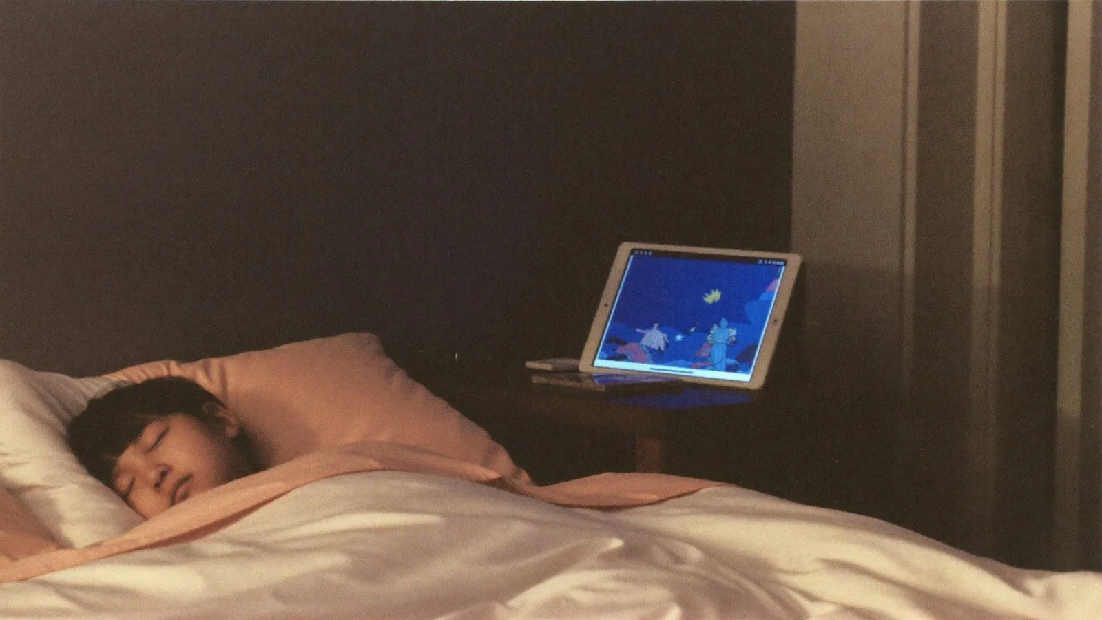 A child asleep, a tablet glowing softly on the nightstand